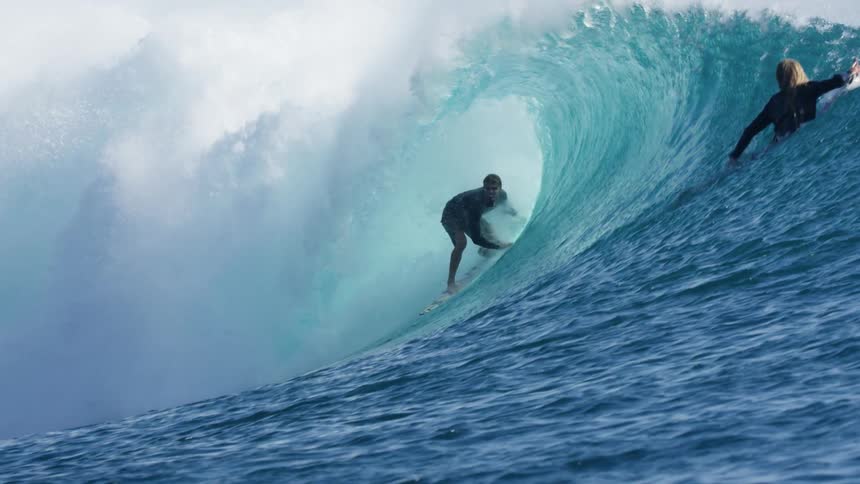 Surfer rides an ocean wave with a surfboard next to land