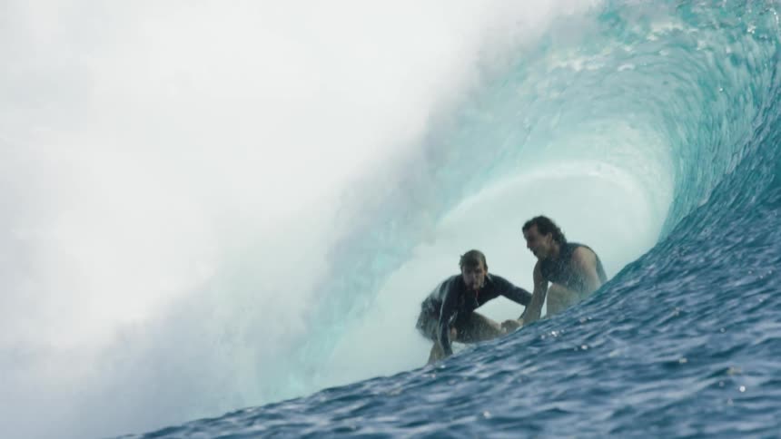 Surfers barrel surfing in the ocean as other surfers watch