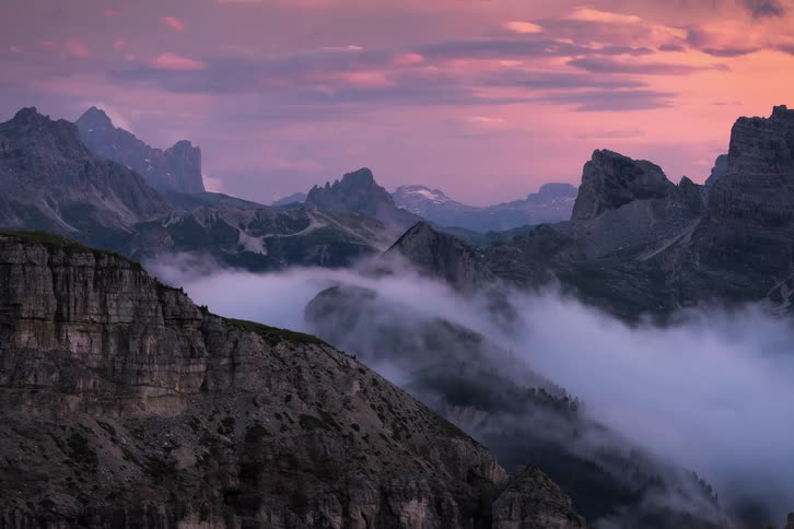 A fog bank flows over the side of a mountain