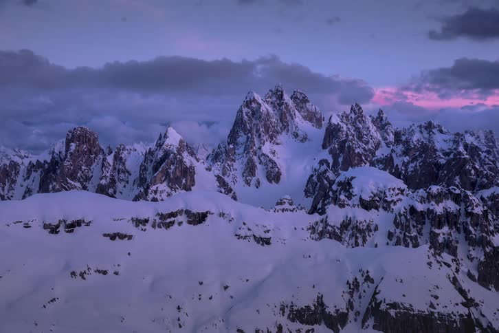 Snow capped mountains landscape with clouds floating in the background at dusk
