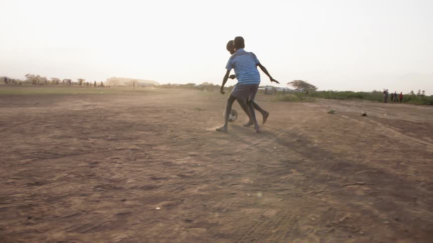 Teenagers play soccer barefoot on the sand at sunset