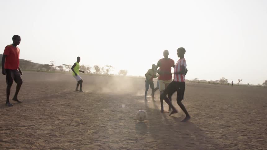 Group of teenagers play soccer barefoot on the sand at sunset