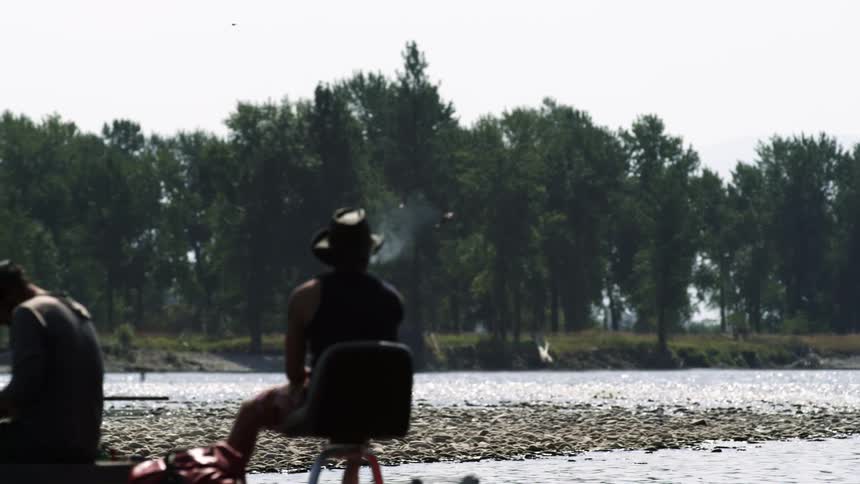 Two men sitting on the shore of a river fishing
