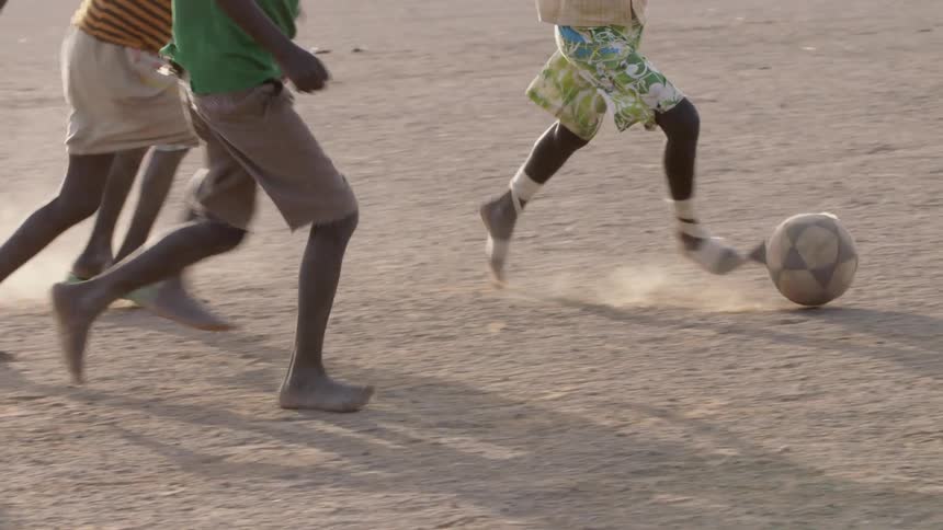 The legs of kids kicking and playing with a soccer ball in the dirt