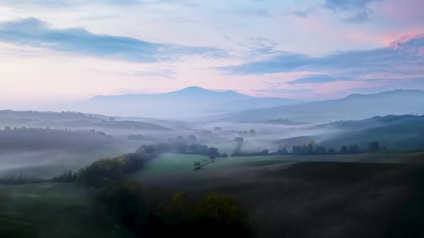Fog hovers over fields and farmland in a mountain valley