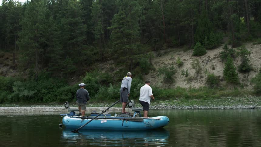 Three men in a raft on a lake fishing with trees and the sky in the background