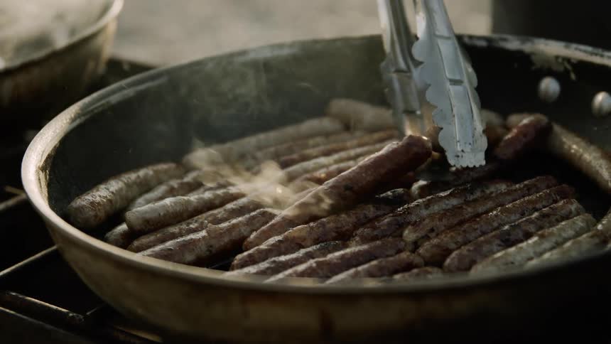 A pan full of sausage links is cooked on a grill outdoors