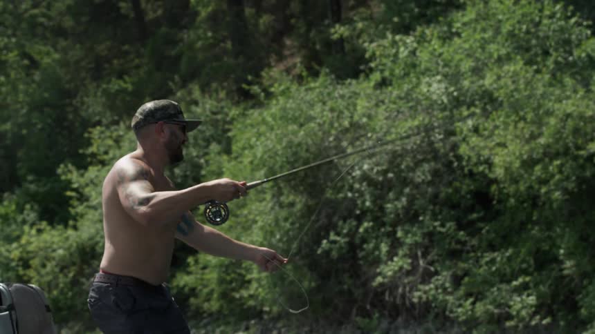 A man with a fishing rod fly fishing with trees in the background