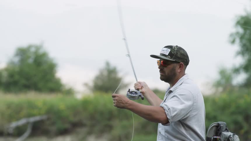 Man with a green cap sunglasses and a beardcasts a fishing line to catch fish