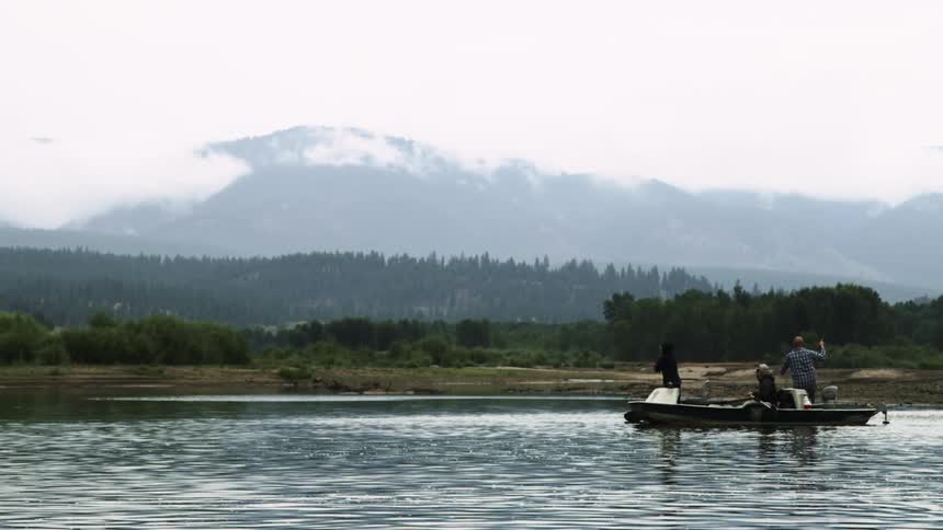People on a boat fishing in a lake close to cloud covered mountains