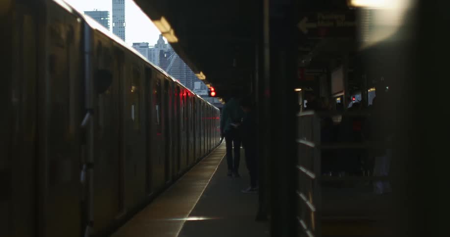 People walk and wait at an elevated train station in a city
