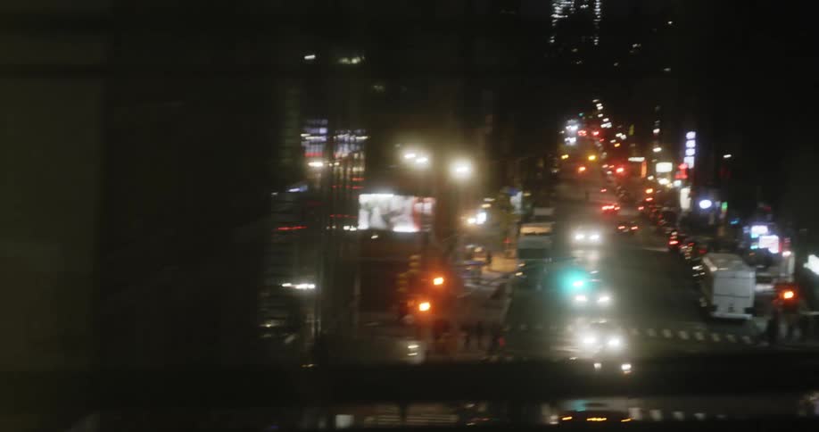 A fence on a bridge gives way to a view of a city street filled with traffic at night