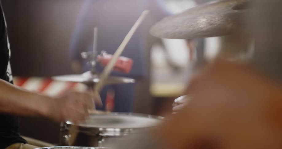 A drummer sitting at a drum set striking it with his drum sticks