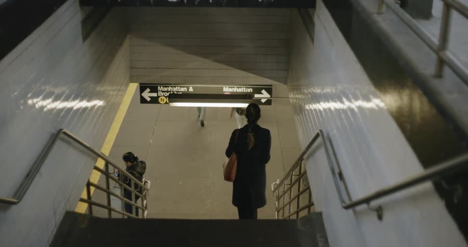 A white woman takes the stairs down into a city subway system