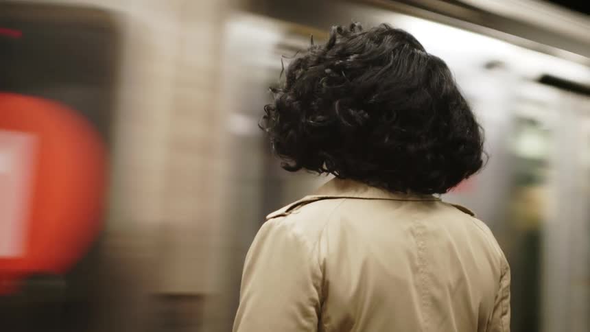 Woman stands in a subway station waiting for a train to stop