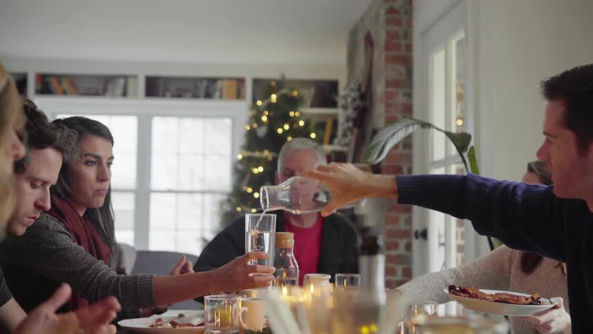 Family of six sitting at the dining table on christmas eating while male pours water into females glass from across the table