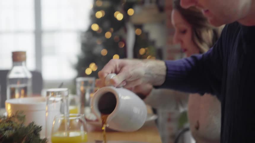 A man pouring syrup onto his plate with a woman and a christmas tree in the background