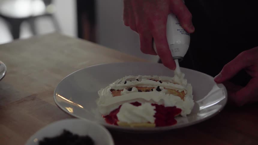 A person spraying whipped cream on a pastry on a plate