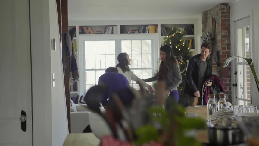 People in the living room where a man closes the door and two women hug