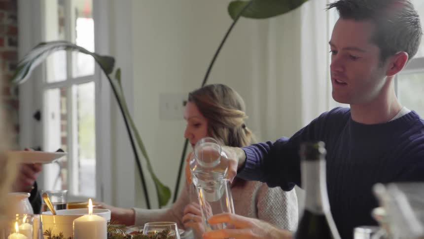 A man sitting at a table with others pours water in a glass