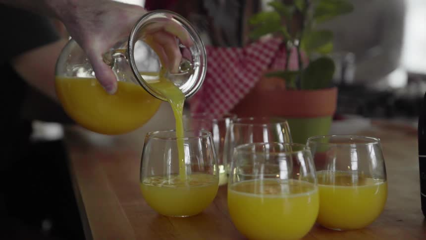 Man pours orange juice on glasses containing liquor at home