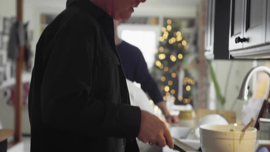 A father stands near his son as he cooks pancakes in a kitchen