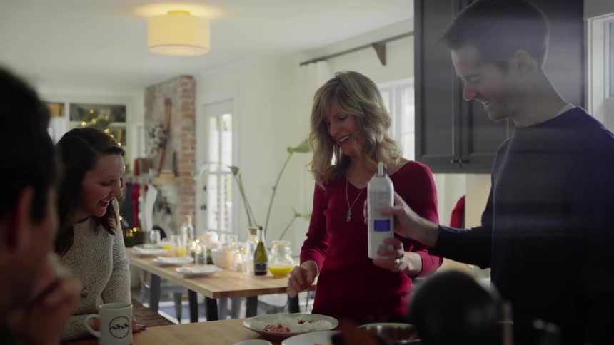 A white woman laughs as she sprays whipped cream on a plate while her family watches