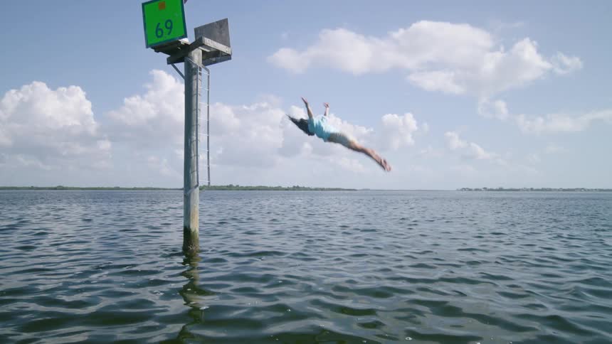A white person dives off of an elevated platform into a body of water