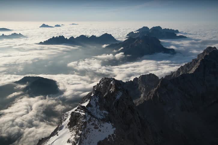 Clouds flow like water around mountain peaks under blue sky