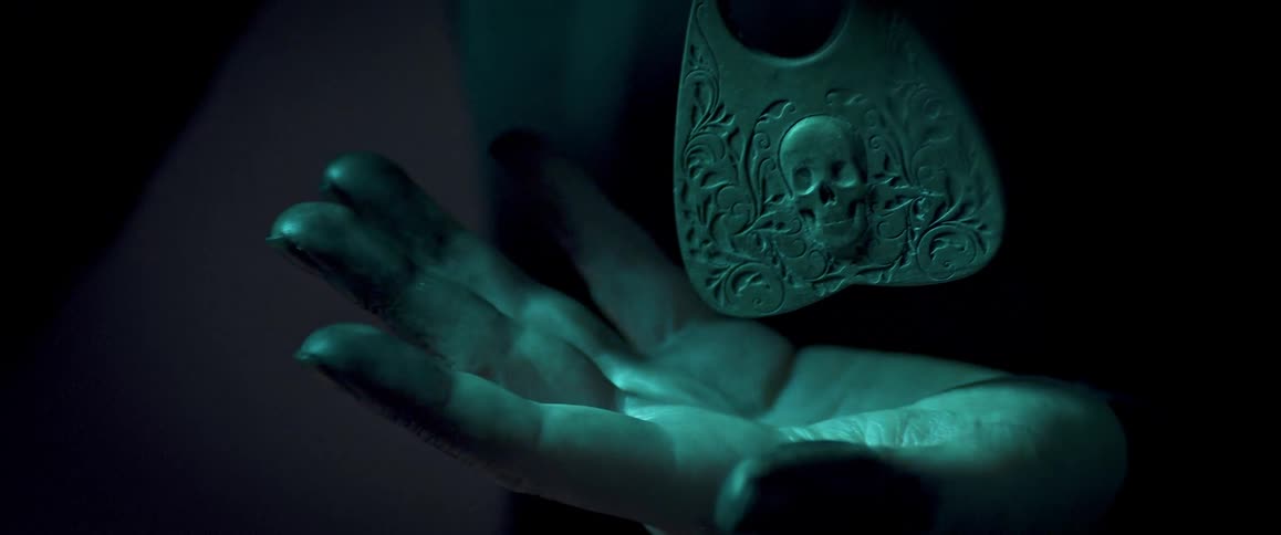 A woman opens and closes her palm underneath a large earring with a skull carving