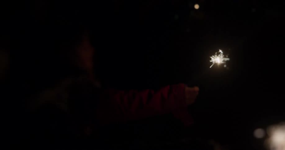 A young child blows on a sparkler and then waves it around