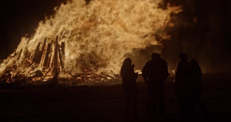 A group of people stand and watch a fire burning