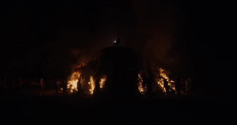 People stand around a large bonfire as fireworks go off