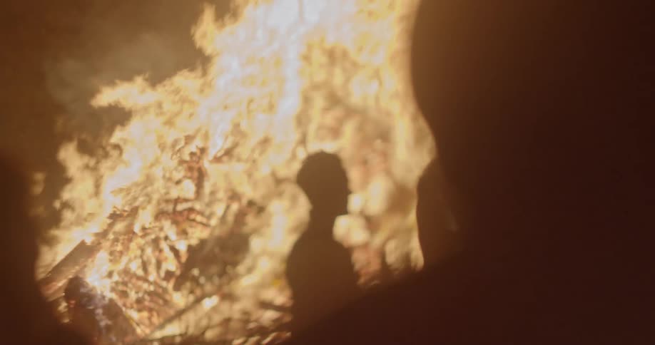 People move around outdoors near a giant bonfire