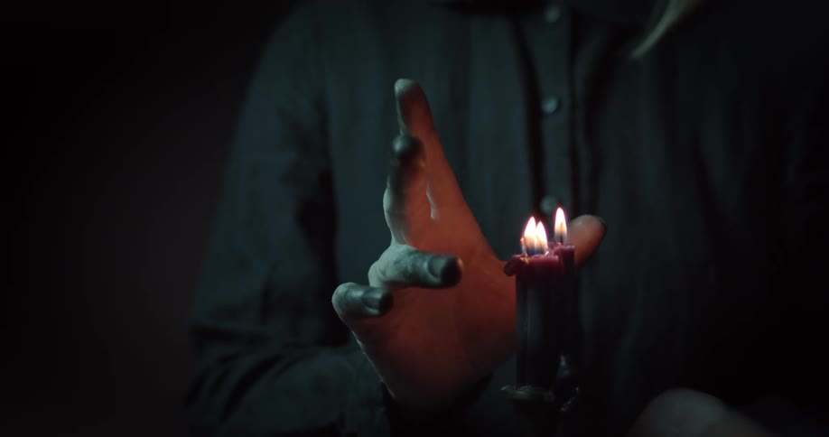 A white man puts his hand close to flames on candles
