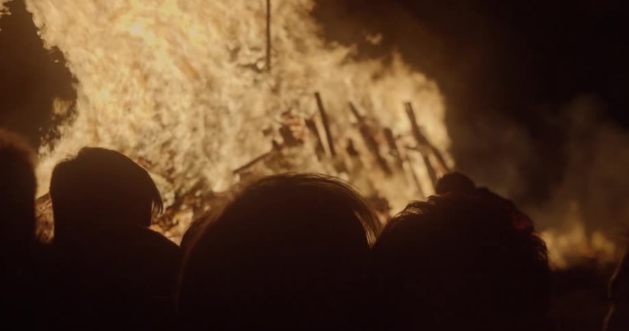 A crowd of people watching a large bonfire at night