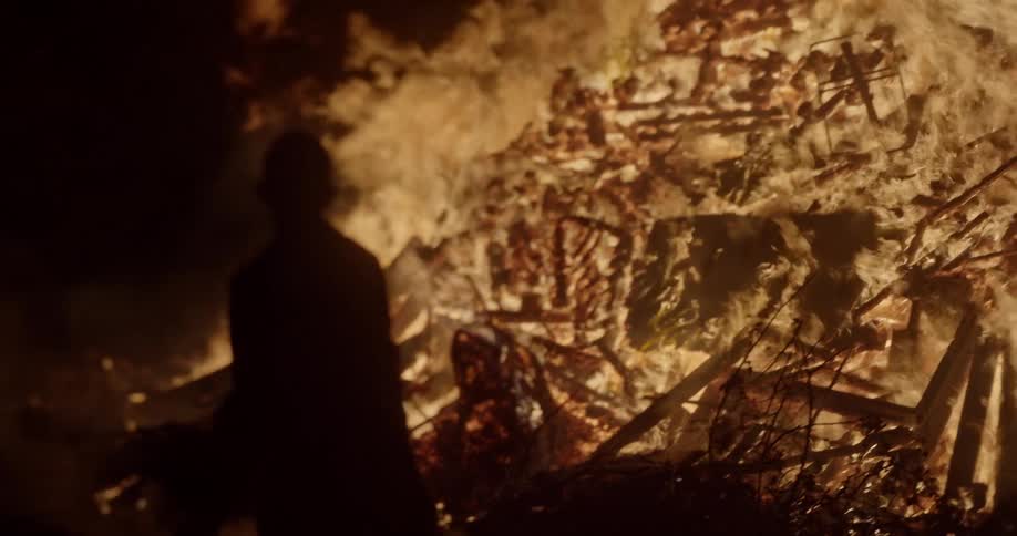 A male throws an object into a roaring bonfire