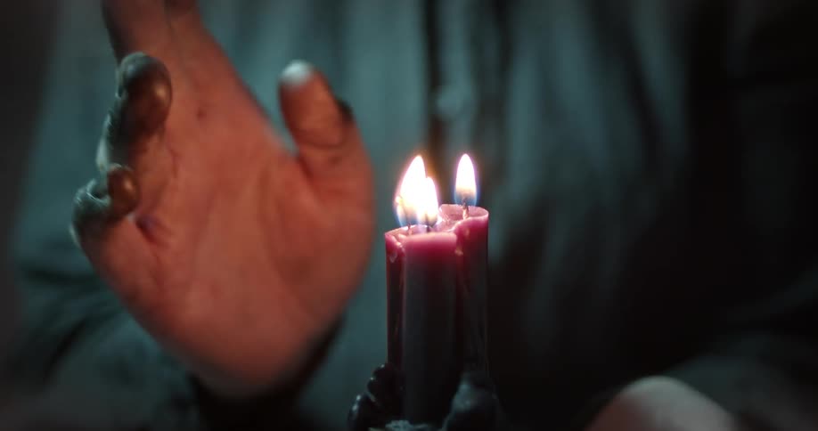 A person uses their hand to nearly extinguish three candle flames