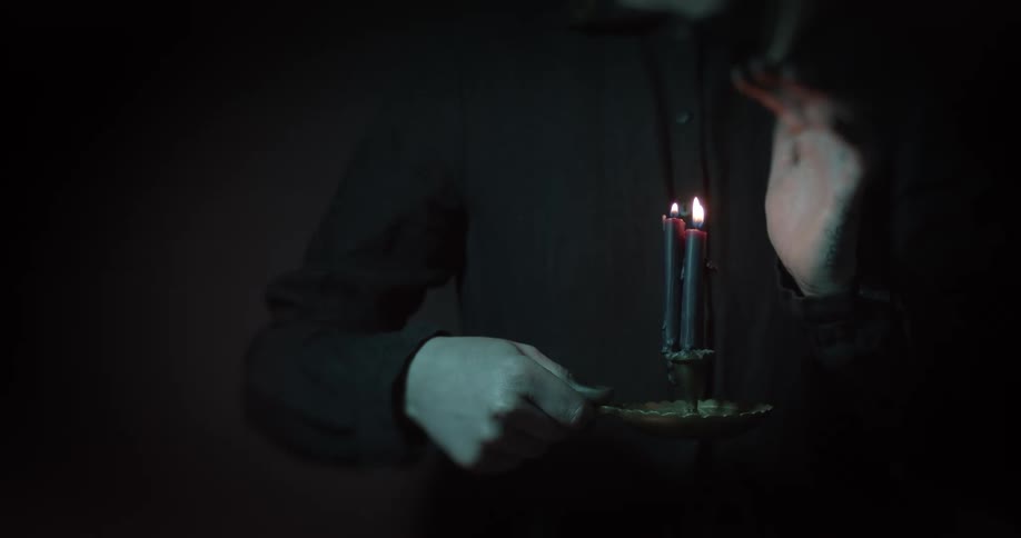 A person holding candles on a candlestick while waving their hand close to the flame
