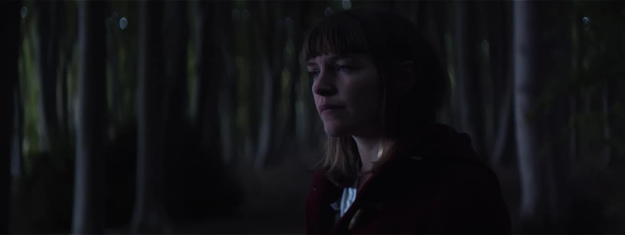 A teenager stands in a dark forest