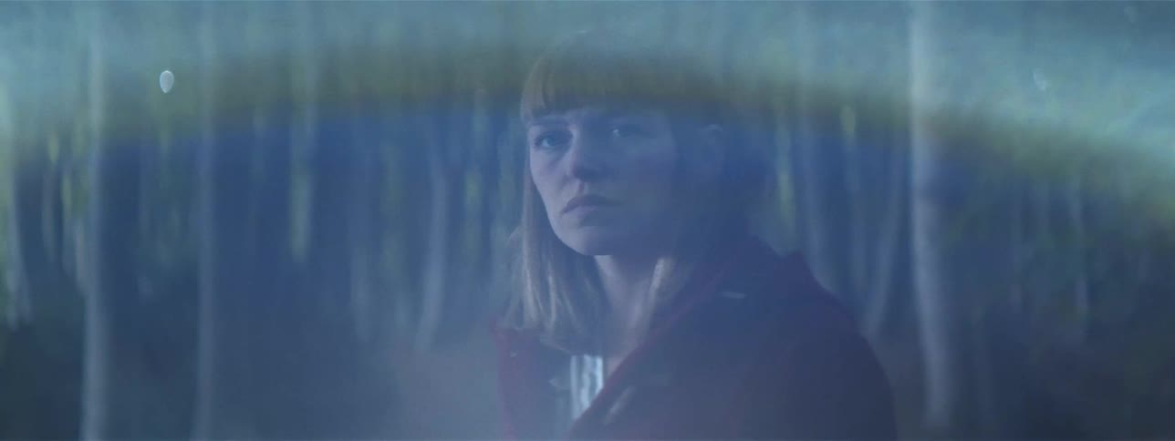 A white woman stands in the forest and looks off into the distance