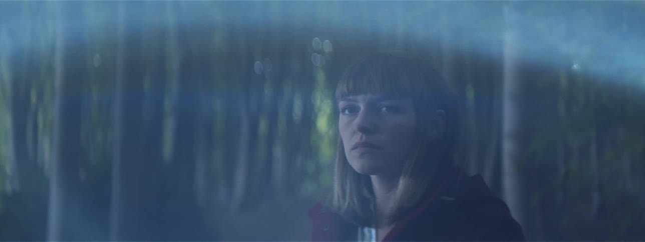 A young woman stands in a dark forest as a bright light shines