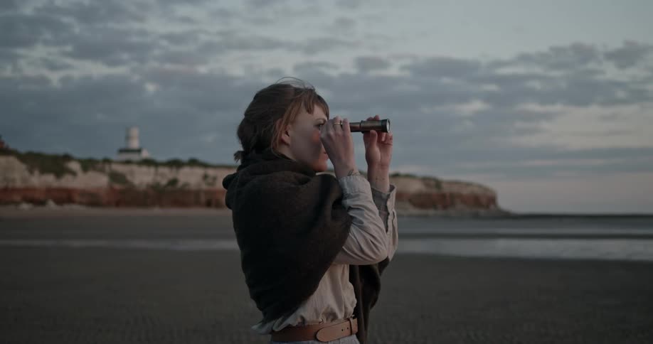 A young woman stands on the beach and looks through a telescope