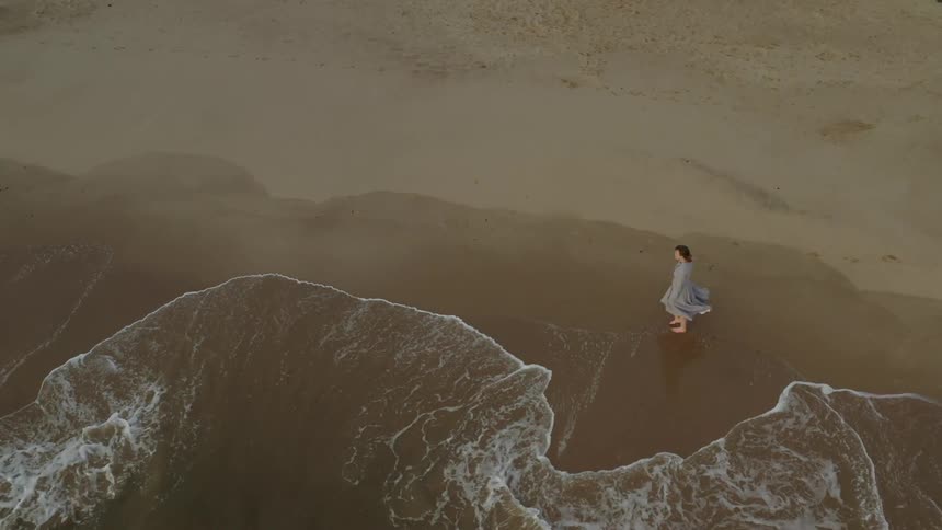 Woman walks barefoot along the shoreline as the waves roll in