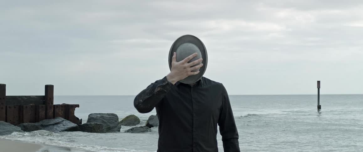 Person posing with hat over face at shoreline on the beach