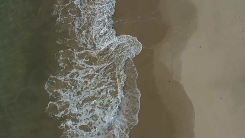Aerial top down view of sea waves gently crashing on the sand of a beach
