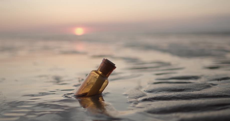 A bottle with a note in it halfway buried in the sand with the sky in the background