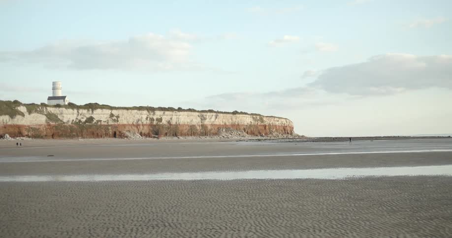 Three people walk across a large beach area near cliffs