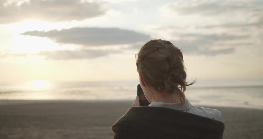 A woman looks at her smartphone while standing on a beach