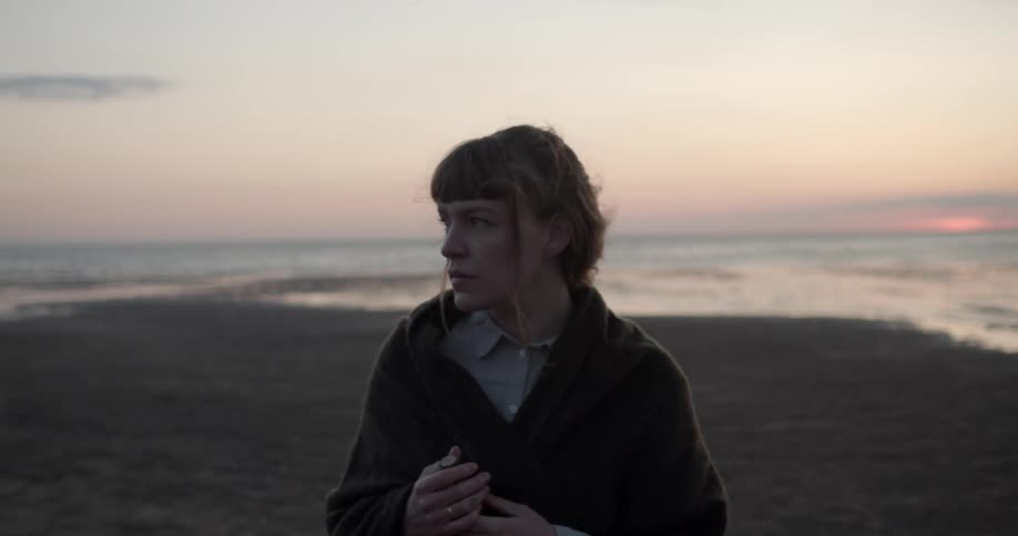 A woman walks along a beach looking sad